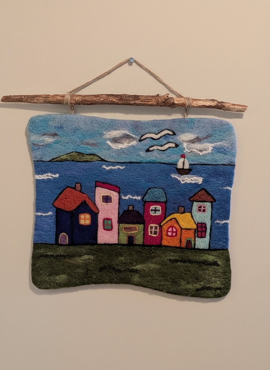 Handmade wall art with colorful houses and a boat on a blue background, hanging on a branch.